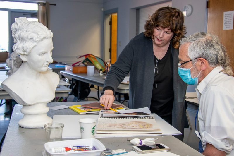 An instructor and student work on a painting together.